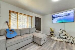 Ein Wohnzimmer mit einem Ecksofa, einer blauen Gitarre, einer Tigerstatue und einem Fernseher, der ein Landschaftsbild zeigt.