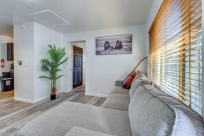 A living room with a grey sofa, a potted plant, a guitar leaning against the wall, and a framed picture of lions. - Tucson Home Base Near I-10, 5 Mi to Downtown! (Tucson)