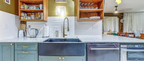 Una cocina con estantes de madera empotrados, un lavamanos de acero inoxidable y un lavavajillas.