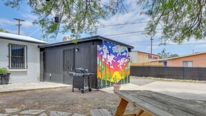 Un petit bâtiment agrémenté d’une fresque colorée, avec un barbecue et une table de pique-nique, le tout situé dans un jardin.