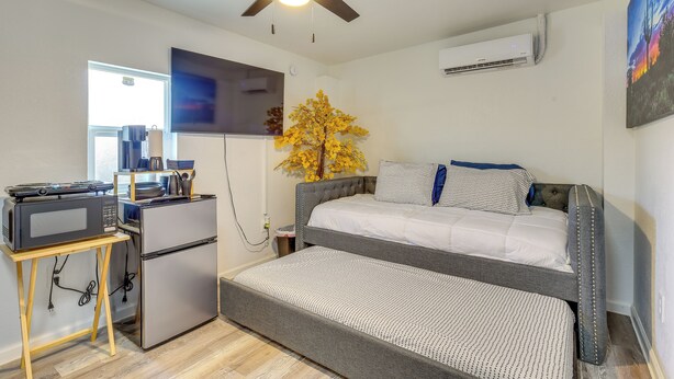 Une pièce de taille modeste comprenant un lit, une petite kitchenette, un ventilateur de plafond et une fenêtre.