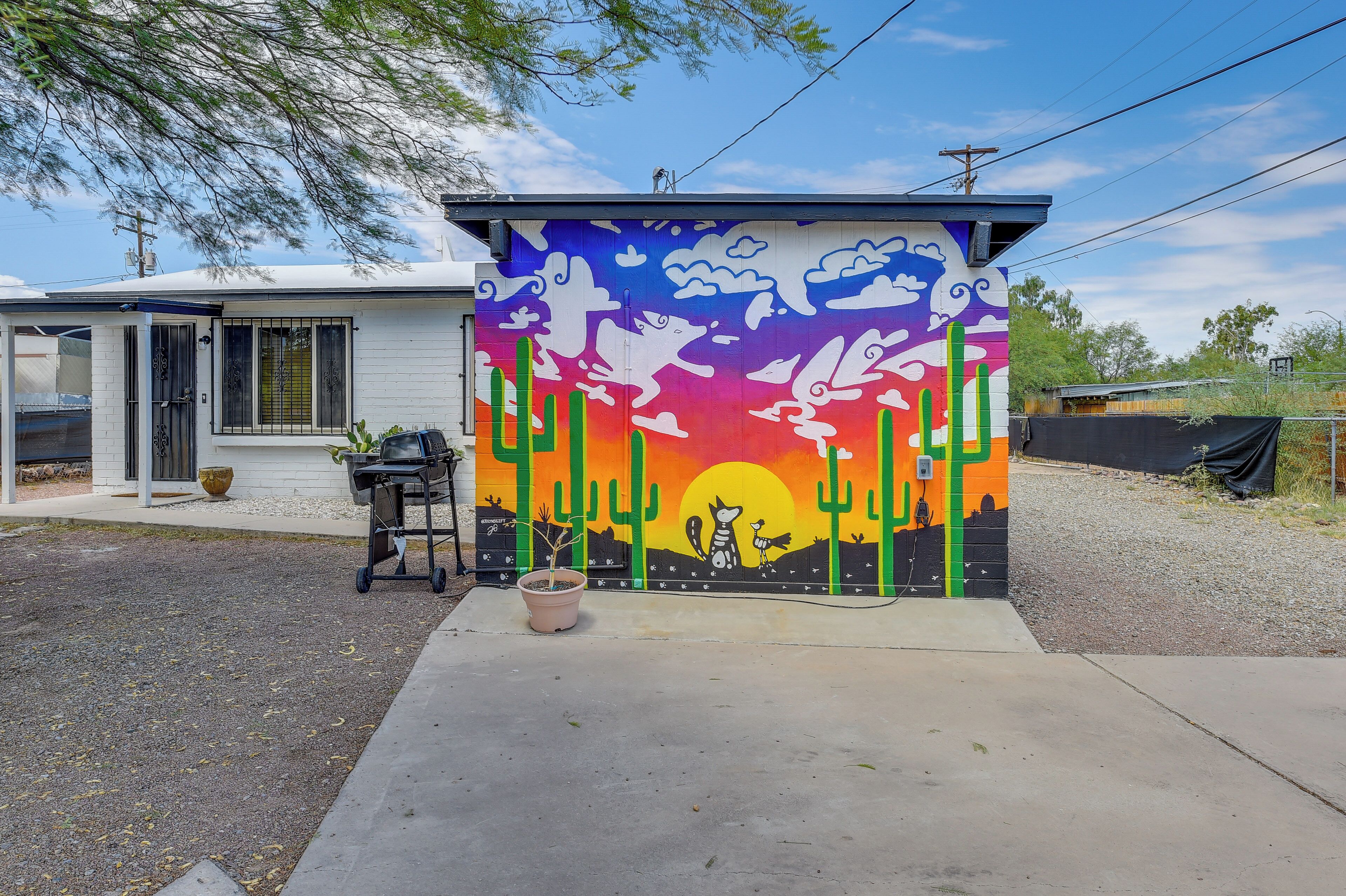 A house with a colorful mural on the exterior wall, a garage door, and a potted plant in the driveway.