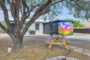 A tree, a wooden picnic table, and a colorful building with a mural.