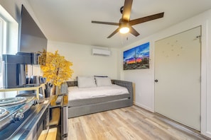 A bedroom with a bed, a ceiling fan, a painting, and a door.