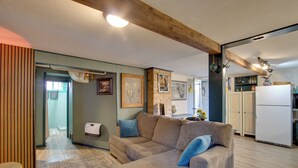 A living room with a sofa, a wooden ceiling beam, a kitchen area with cabinets, and a refrigerator. - Walk to SSU & Shakespeare Fest! Colorful Retreat (Cedar City)