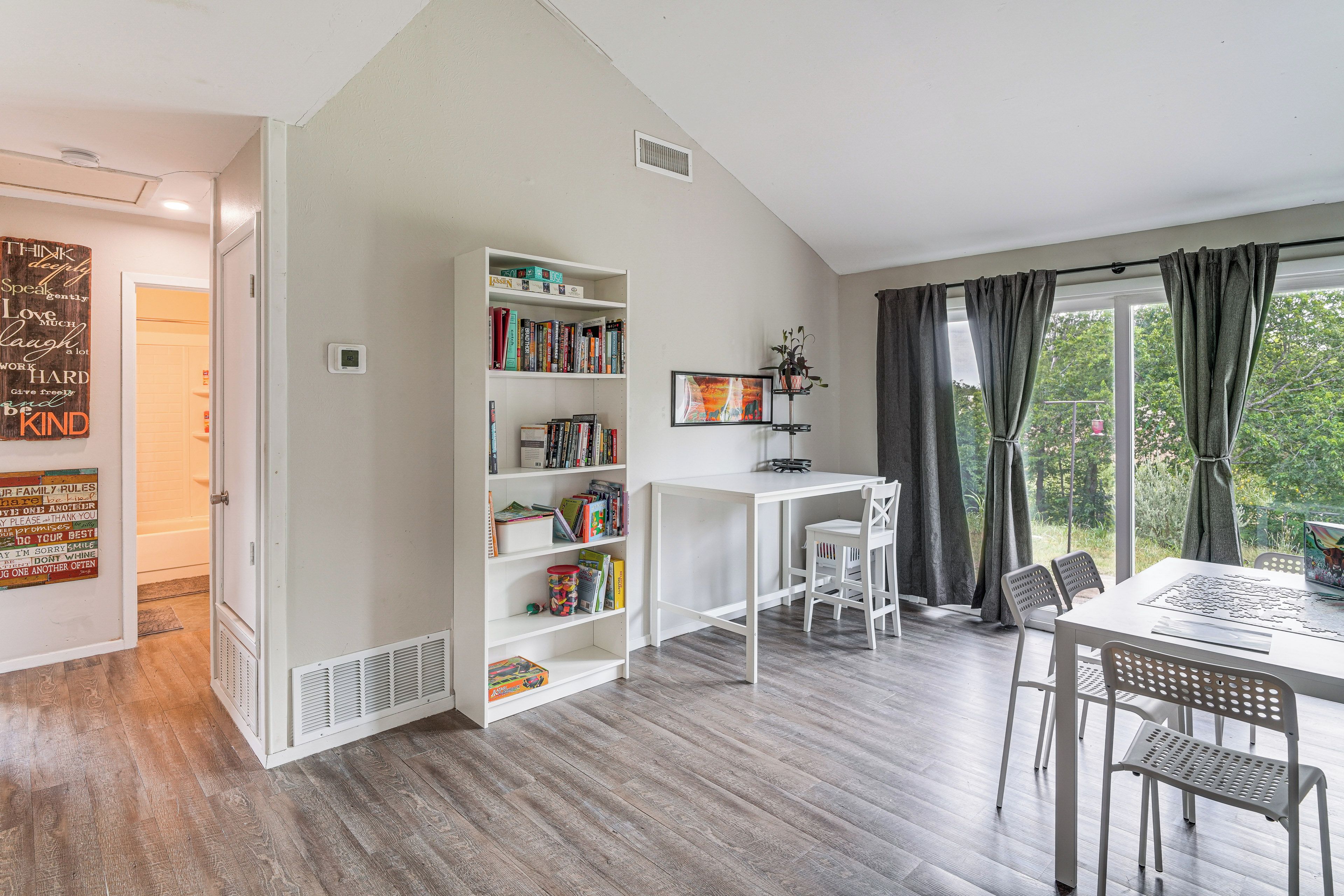 A room with a white bookshelf, a desk, and a dining area with chairs.