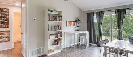 A room with a white bookshelf, a desk, and a dining area with chairs.
