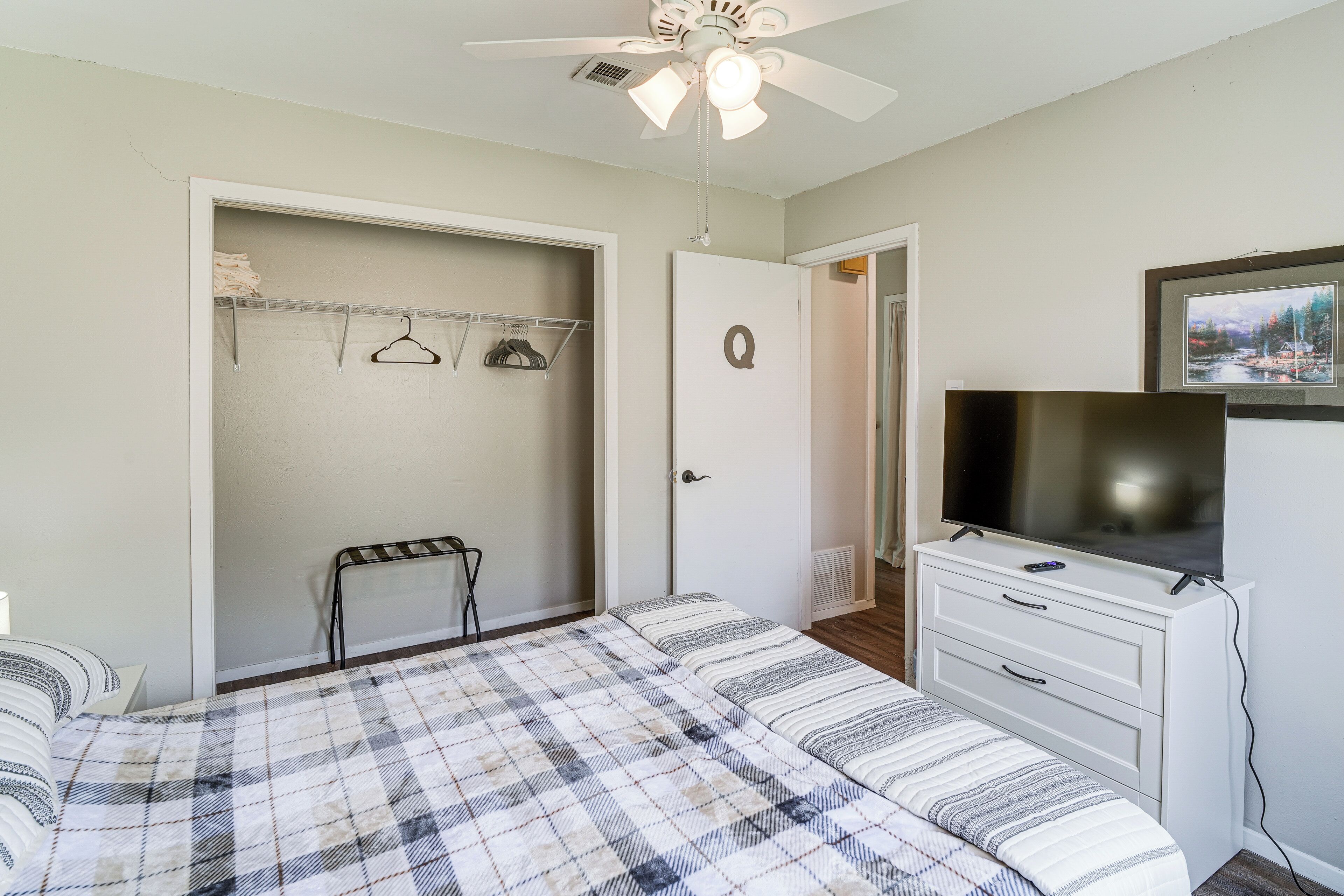 Un dormitorio con cama, televisor, armario y ventilador de techo.