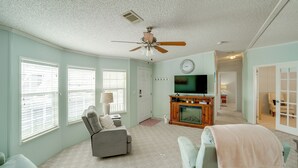 Ein Wohnzimmer mit Deckenventilator, Fernseher, Kamin und einer Couch.