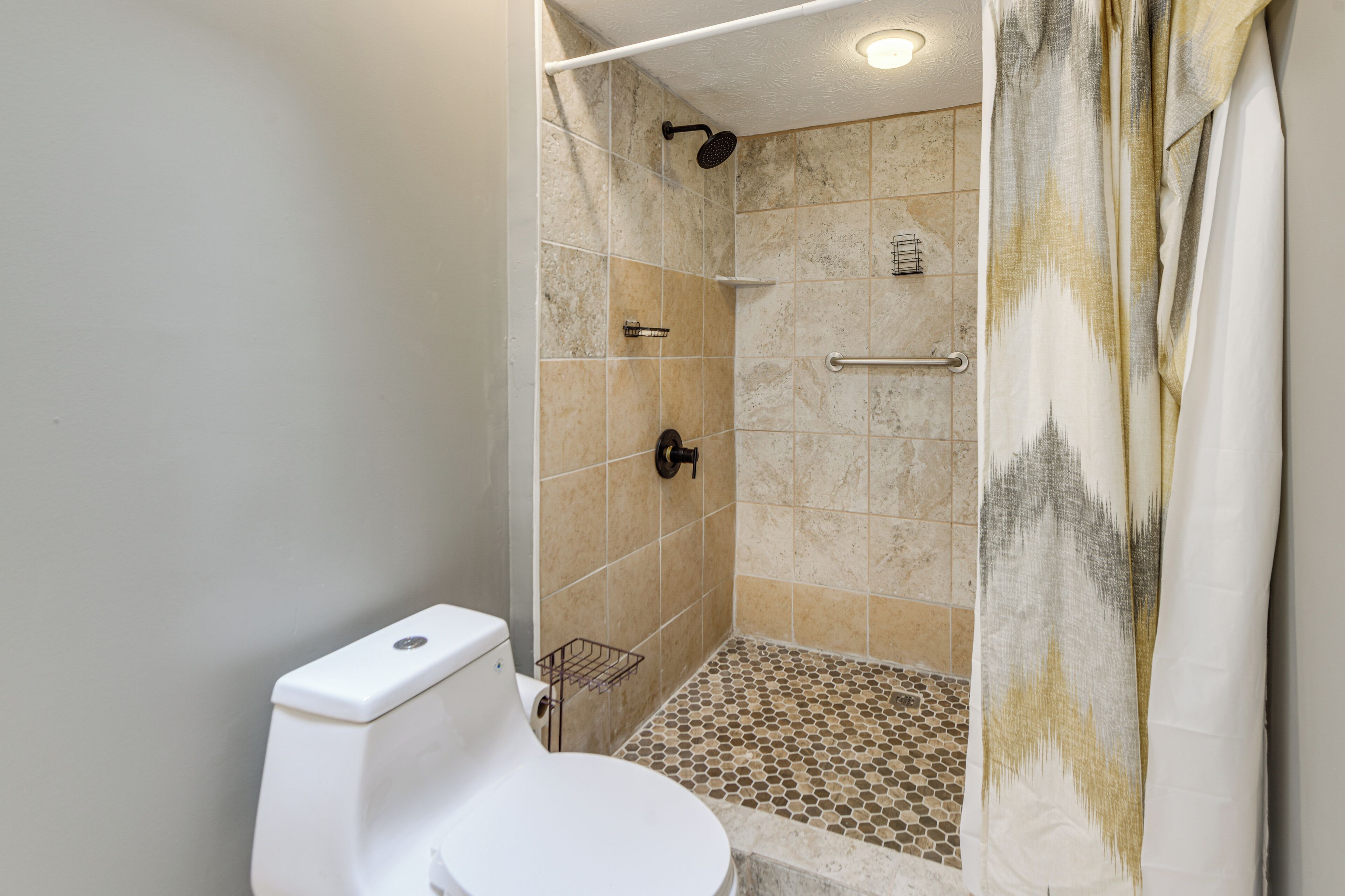 A bathroom with a shower, toilet, and tiled floor.