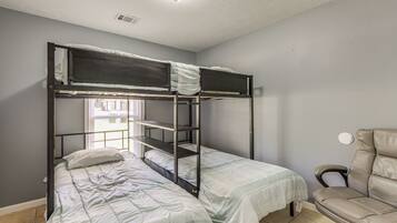 A bunk bed room with a window, a chair, and a ceiling light fixture.