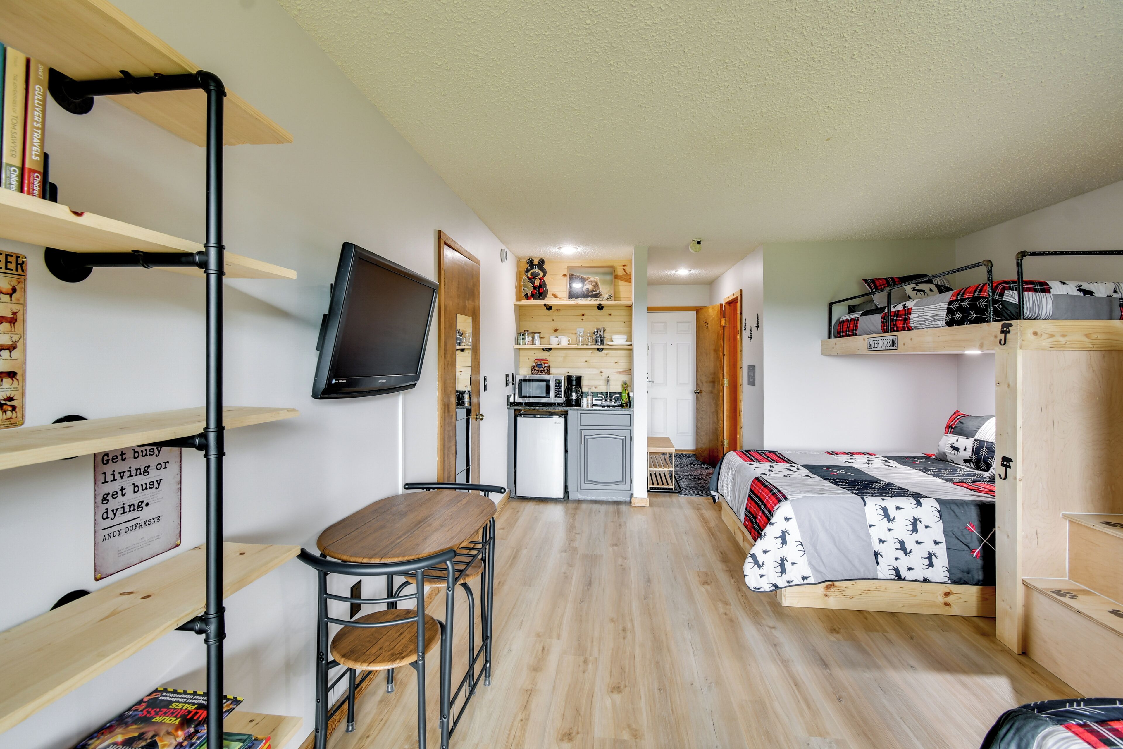 A compact room with a bed, a small kitchenette, a dining area, and a TV mounted on the wall.