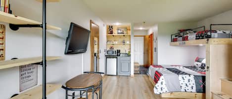 A compact room with a bed, a small kitchenette, a dining area, and a TV mounted on the wall.