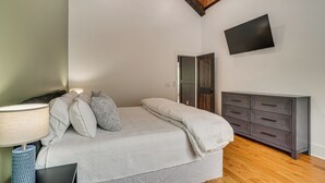A bedroom with a bed, bedside lamp, dresser, TV, and a door. - Luxe 4BR Cabin at Innsbruck Resort in Helen (Helen)
