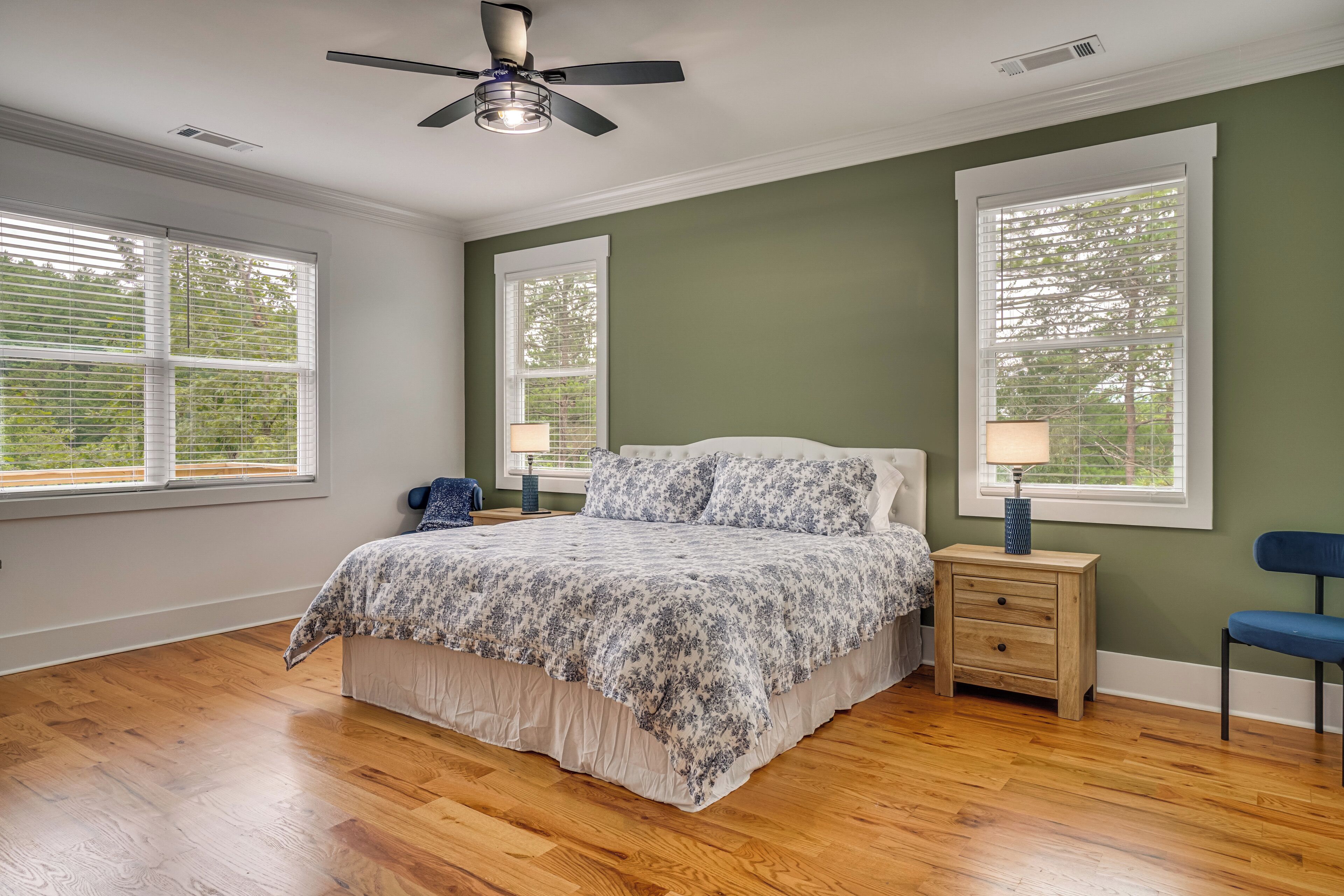 A bedroom with a bed, two bedside tables, a ceiling fan, and large windows.