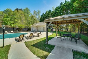 Ein Garten mit Pool, Liegestühlen, einer überdachten Terrasse und einem kleinen Gebäude.
