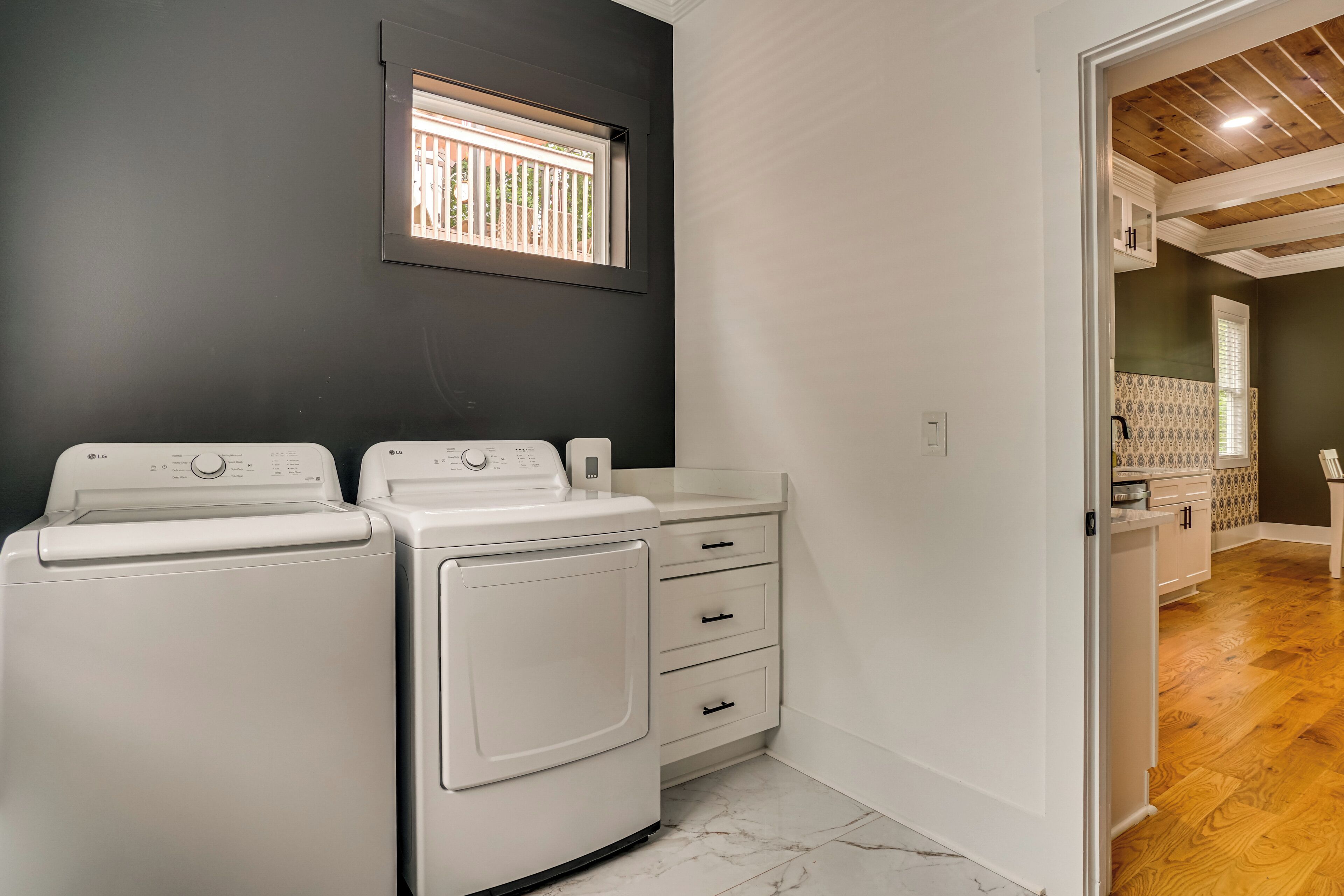 A laundry room with two white washing machines, a small window, and a wooden floor.