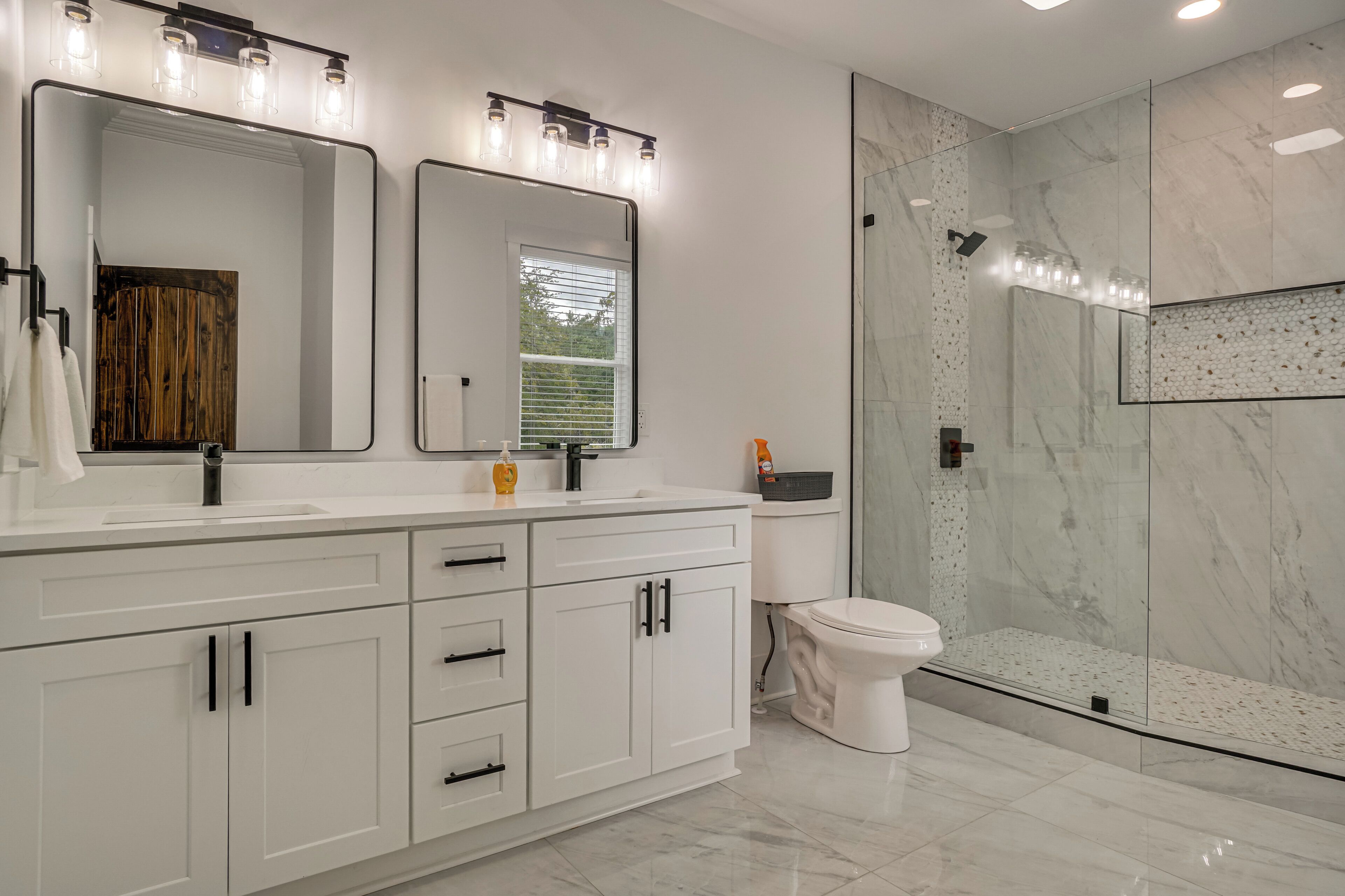 Un baño moderno con tocador blanco, espejos dobles y cabina de ducha con vidrio.