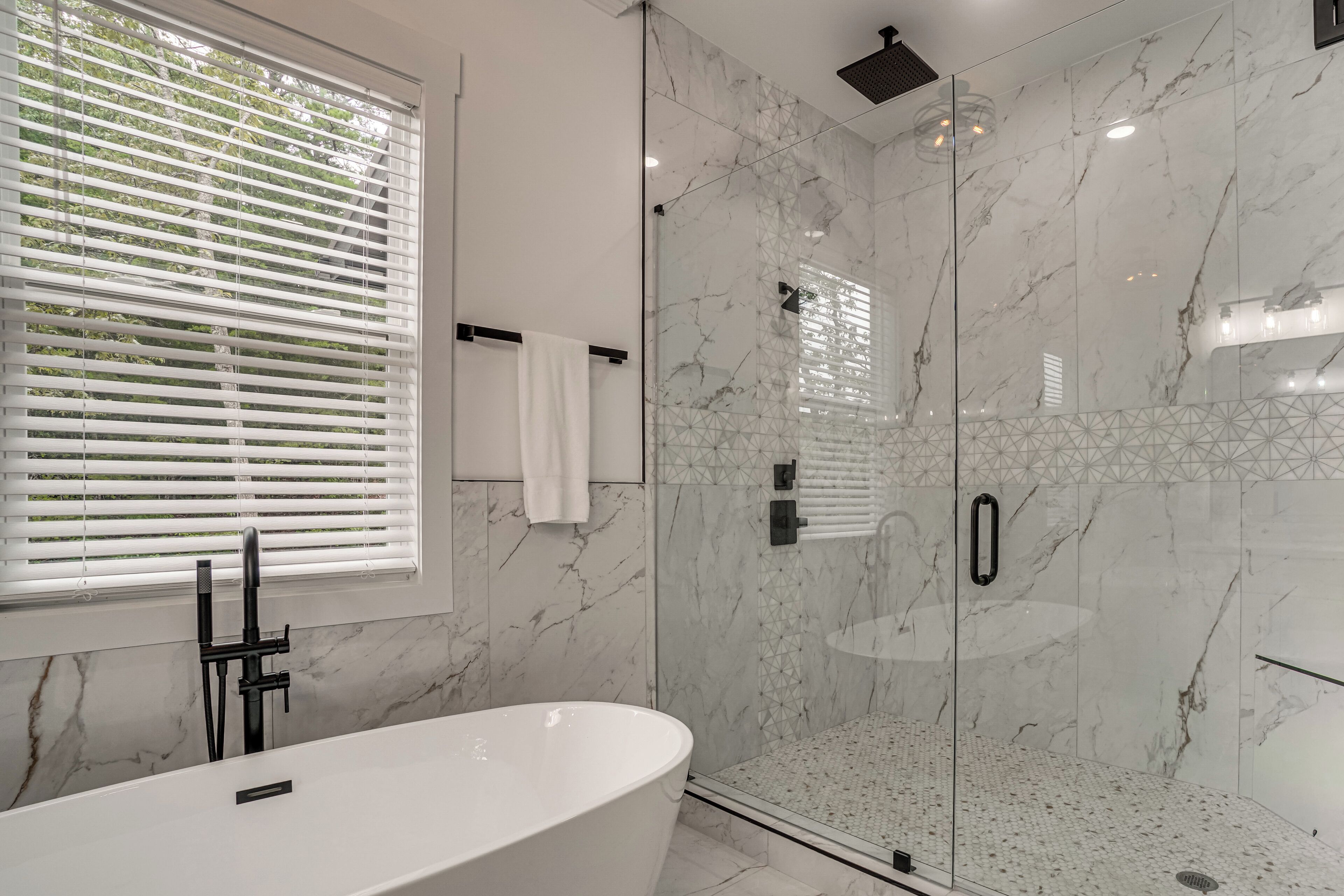 A modern bathroom with a freestanding bathtub, a glass-enclosed shower, and a window with blinds.