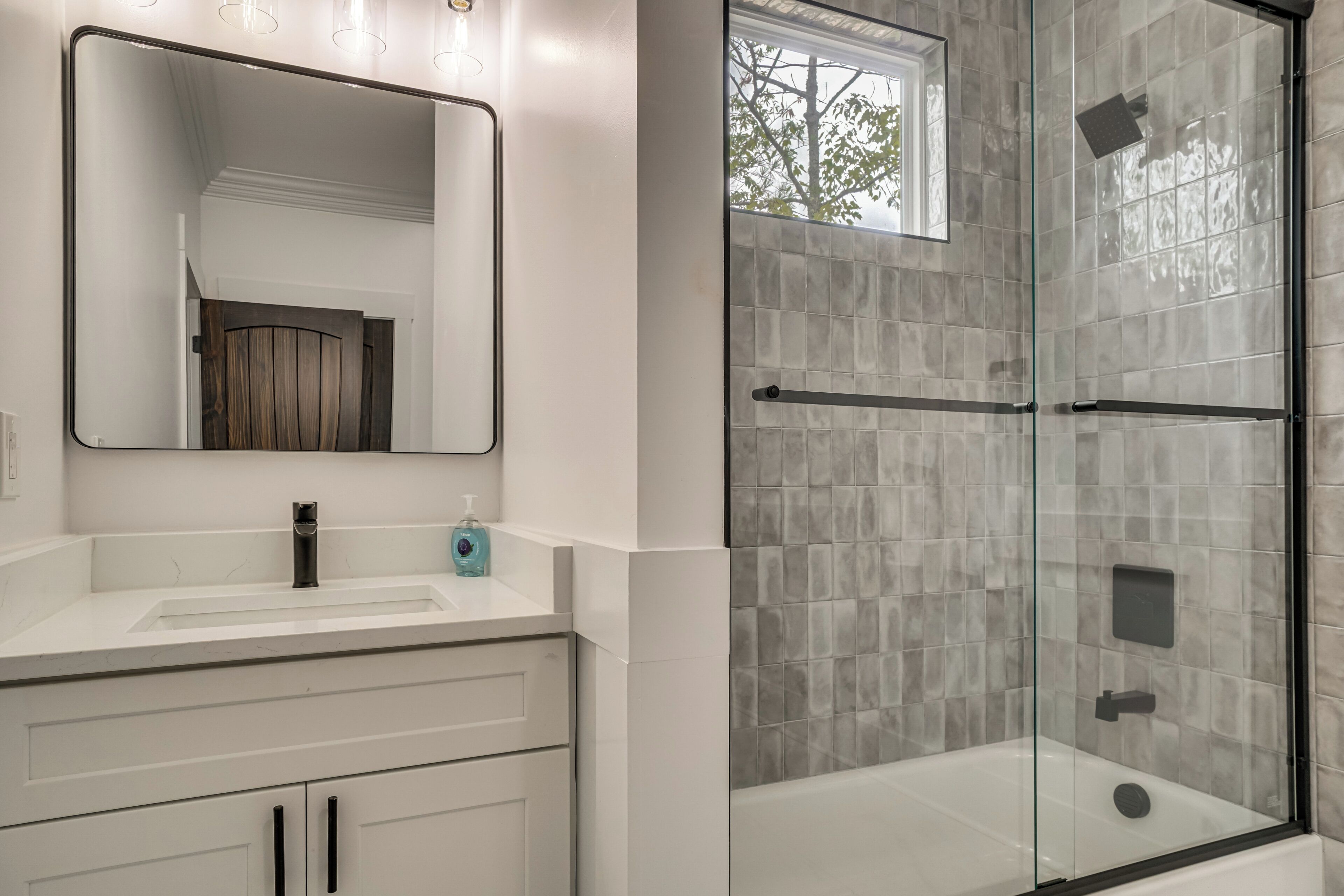 A modern bathroom with a glass-enclosed shower, a large mirror, and a white vanity.
