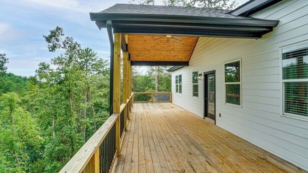 A wooden deck with a railing, a covered area, and a view of a forested area. - Luxe 4BR Cabin at Innsbruck Resort in Helen (Helen)