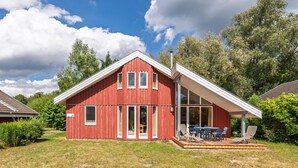 A red two-story house with a covered patio and a large window. - Gemutliches Ferienhaus mit Garten und Terrasse im Hafendorf Muritz (Rechlin)