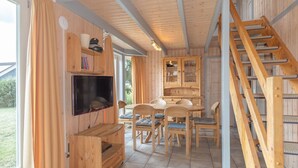A wooden interior with a TV, dining table, chairs, and a staircase. - Gemutliches Ferienhaus mit Garten und Terrasse im Hafendorf Muritz (Rechlin)
