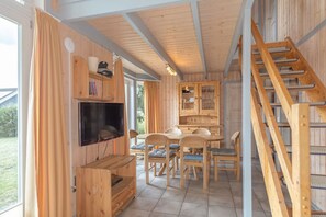 Ein Holzinnenraum mit Fernseher, Esstisch, Stühlen und einer Treppe.