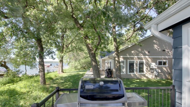 A grill with a control panel, a fenced deck, and a house with a garage in the background. - Family & Angler Friendly! Lake Minnewaska Retreat (Glenwood)