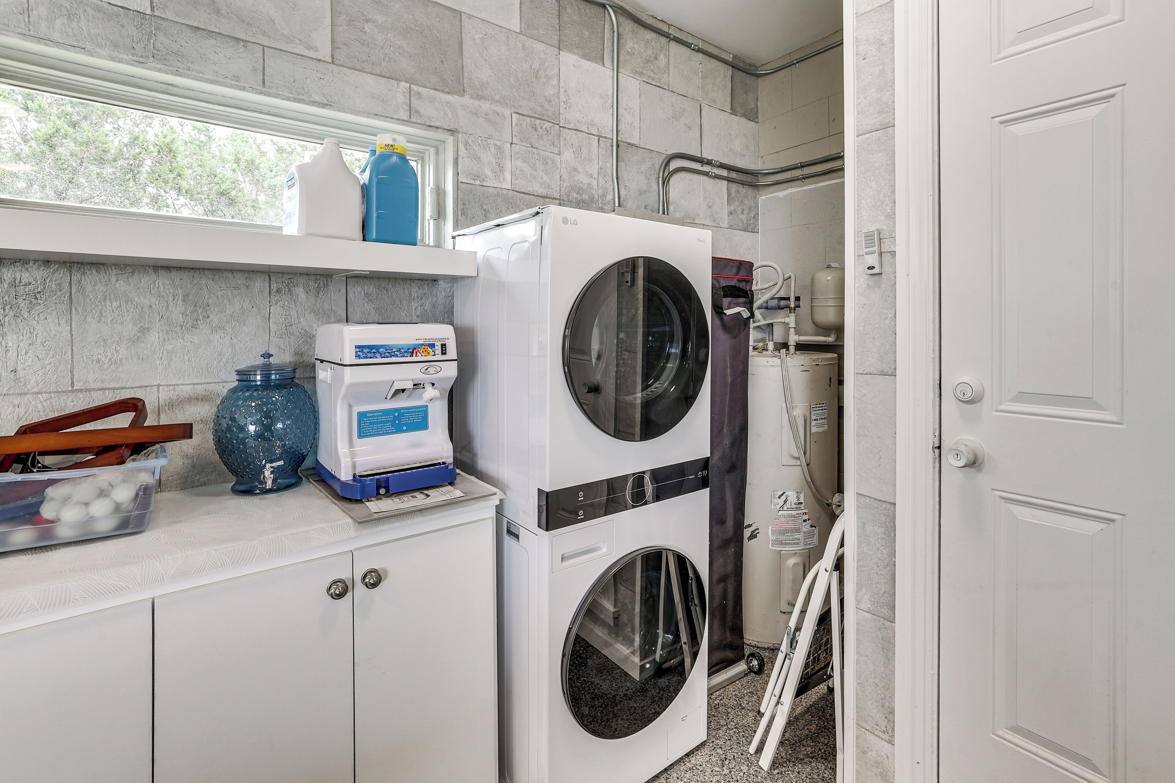 A laundry area with stacked washers and dryers, a water heater, and a window with a view of trees.