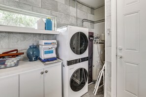 A laundry area with stacked washers and dryers, a water heater, and a window with a view of trees.