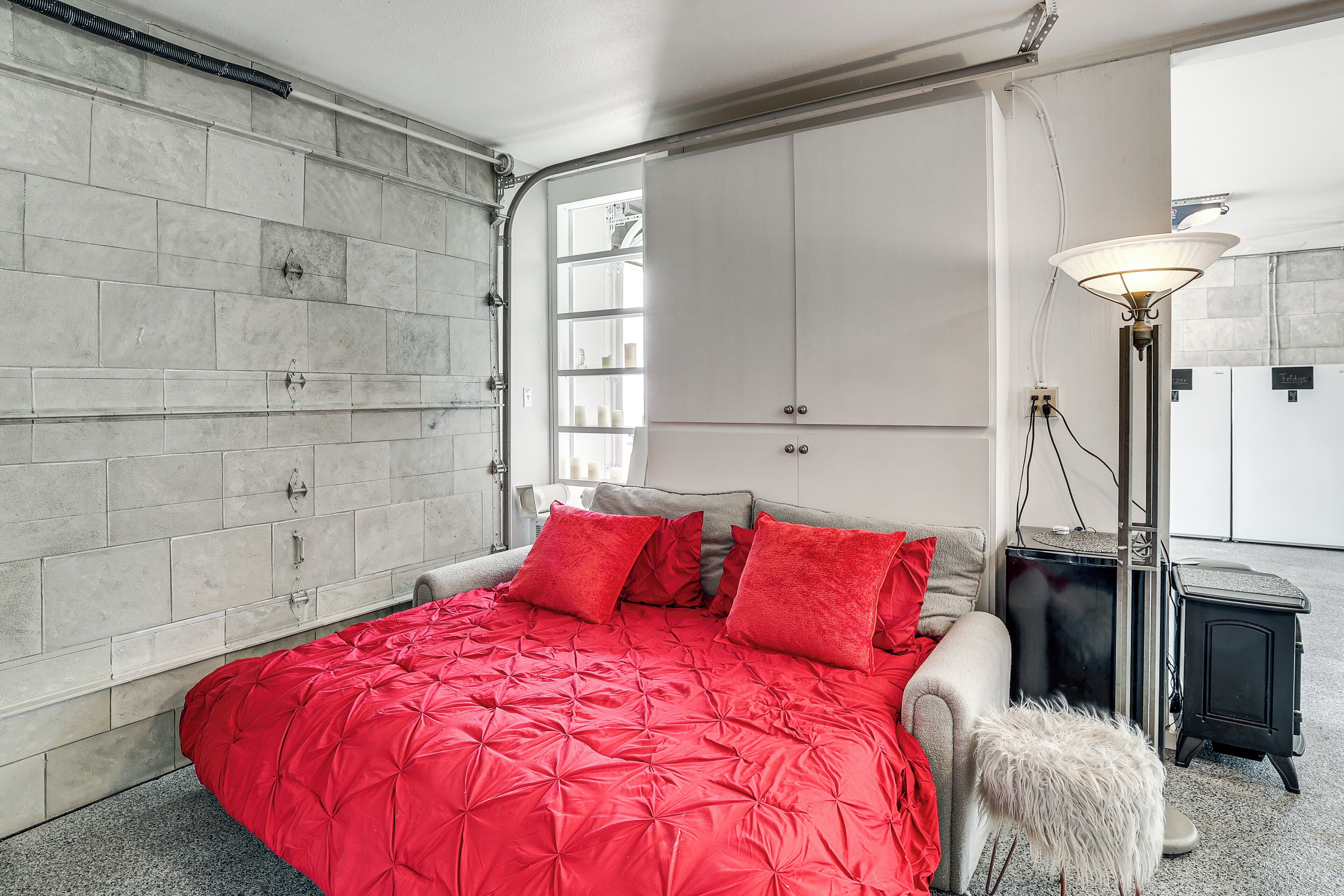 Un dormitorio con una colcha roja, un armario blanco y un calefactor negro.