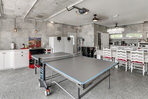 A spacious room with a ping pong table, white cabinets, and a kitchen area with appliances.