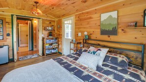 A wooden cabin interior with a bed, a door leading to a bathroom, and a shelf with items. - Ride-in/ride-out North Woods Cabin: On-site Trails (Lee)
