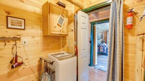 A compact wooden room with a washing machine, a drying rack, a fire extinguisher, and a door leading to another room. - Ride-in/ride-out North Woods Cabin: On-site Trails (Lee)