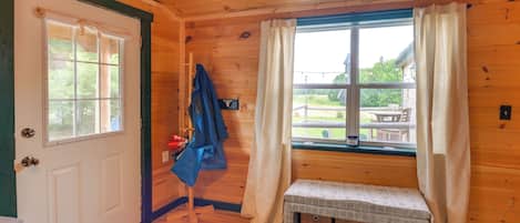 A wooden cabin interior with a bench, a coat rack, and a window with curtains.