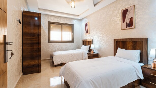 Une chambre d’hôtel avec deux lits, une porte en bois, une fenêtre et un luminaire au plafond.