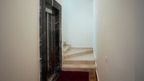 Un escalier recouvert d’une moquette rouge menant à un palier, une porte noire à motifs de marbre et des murs blancs.