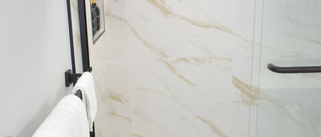 A modern bathroom with a glass-enclosed shower, a white bathtub, and a marble wall.