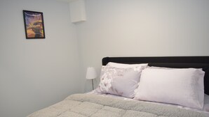 Een slaapkamer met een bed, nachtkastje, lamp en een ingelijste foto aan de muur.