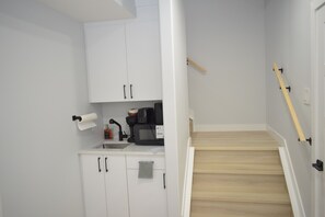 Eine kleine Küche mit weißen Schränken, einer Mikrowelle, einer Kaffeemaschine und einer Holztreppe.
