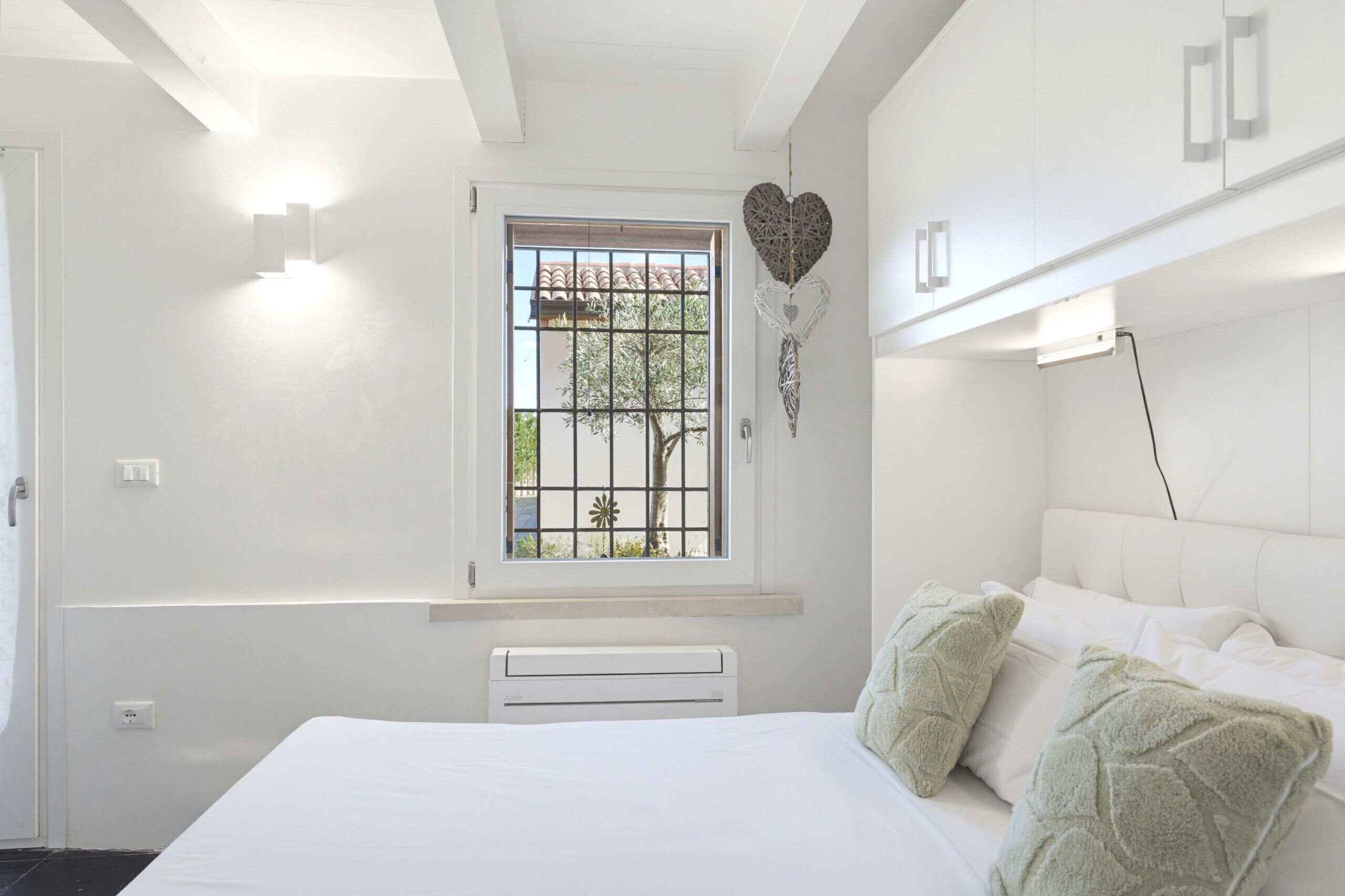 A bedroom with a bed, a window with bars, a radiator, and a wall-mounted light fixture.