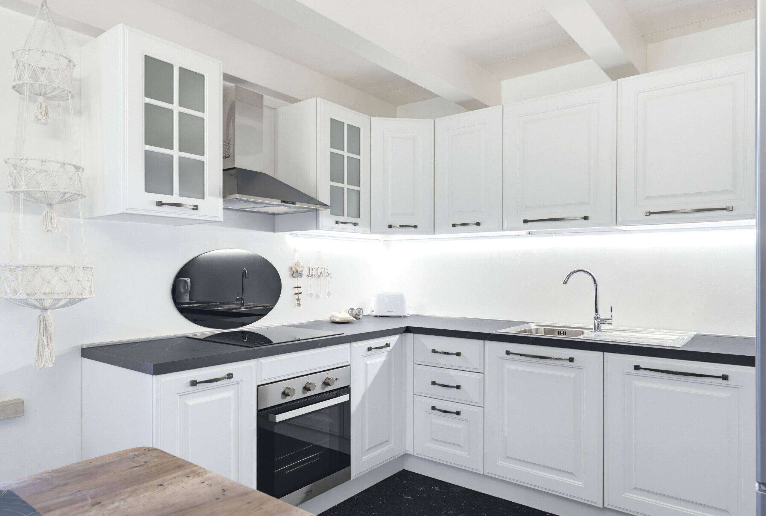A modern kitchen with white cabinets, a black countertop, a built-in oven, and a black range hood.
