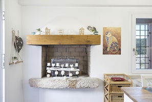 Une cheminée avec un foyer en pierre, une étagère en bois au-dessus et un tableau représentant un chat.
