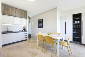 Eine moderne Küche mit weißen Schränken, einem Esstisch mit gelben Stühlen und einem Schwarz-Weiß-Poster an der Wand.