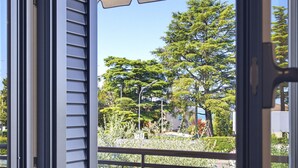 Puerta abierta con vista a un balcón, árboles y una calle.