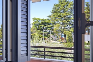 Eine offene Tür mit Blick auf einen Balkon, Bäume und eine Straße.