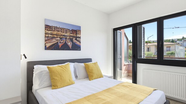 Un dormitorio con cama, un cuadro y vista por la ventana.