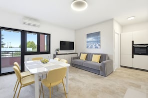 A modern living room with a dining table, sofa, and kitchen area. - Regarda - Basiliko Sport Apartment with tennis and pool (Bardolino)