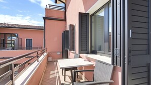 Un balcón con una mesa y sillas, una ventana con persianas y una barandilla.